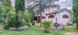A pink building with arched windows and a stone fireplace, surrounded by lush greenery and a well-maintained lawn. - La Casa dei Cuori (Gavorrano)