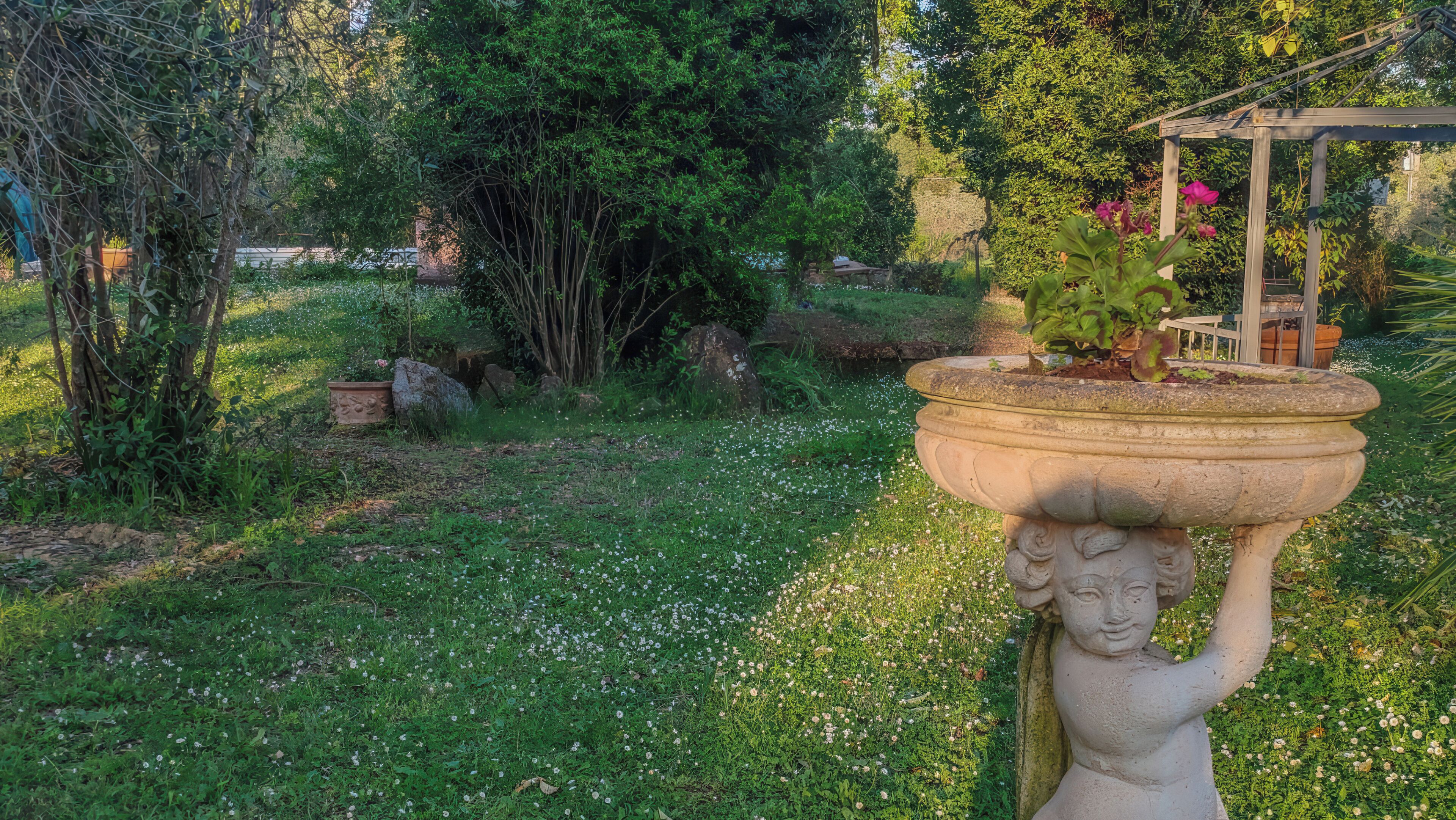 A garden with a stone planter, a statue, and a pergola.