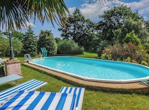 Ein Schwimmbecken mit Holzterrasse, umgeben von Gras und Bäumen, ausgestattet mit Liegestühlen.