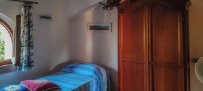 Une pièce comprenant un lit, une armoire en bois, une fenêtre avec des rideaux et un tableau accroché au mur.