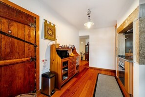 Un couloir doté d’un plancher en bois, un meuble en bois contenant des ustensiles de cuisine, une poubelle et une porte avec une poignée en métal.