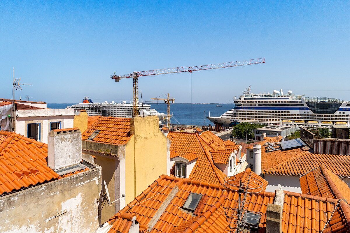A coastal cityscape with traditional terracotta-roofed buildings and two cruise ships docked at the harbor.