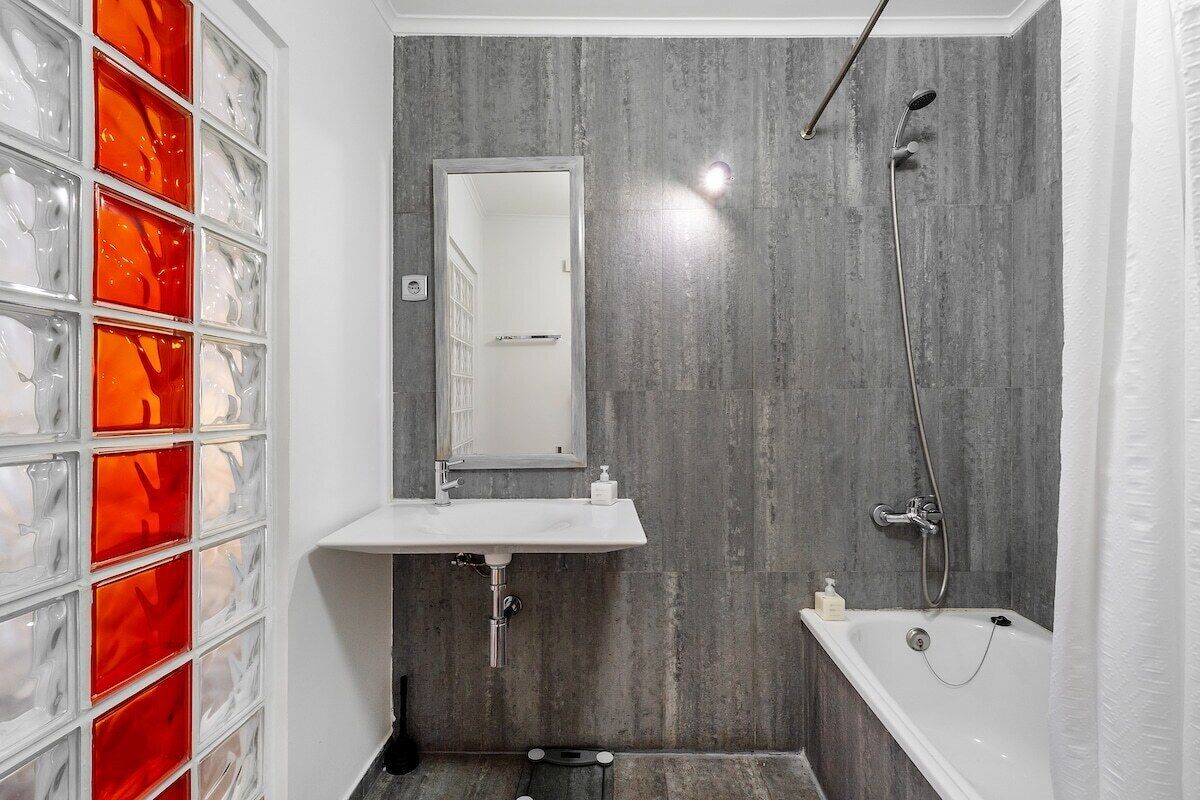 A bathroom with a white sink, a mirror, a shower, and a glass block wall.