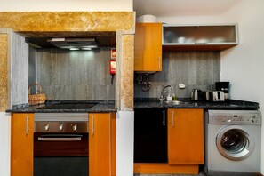 Une cuisine compacte équipée d’un four encastré, d’un lave-linge et d’un petit plan de travail.