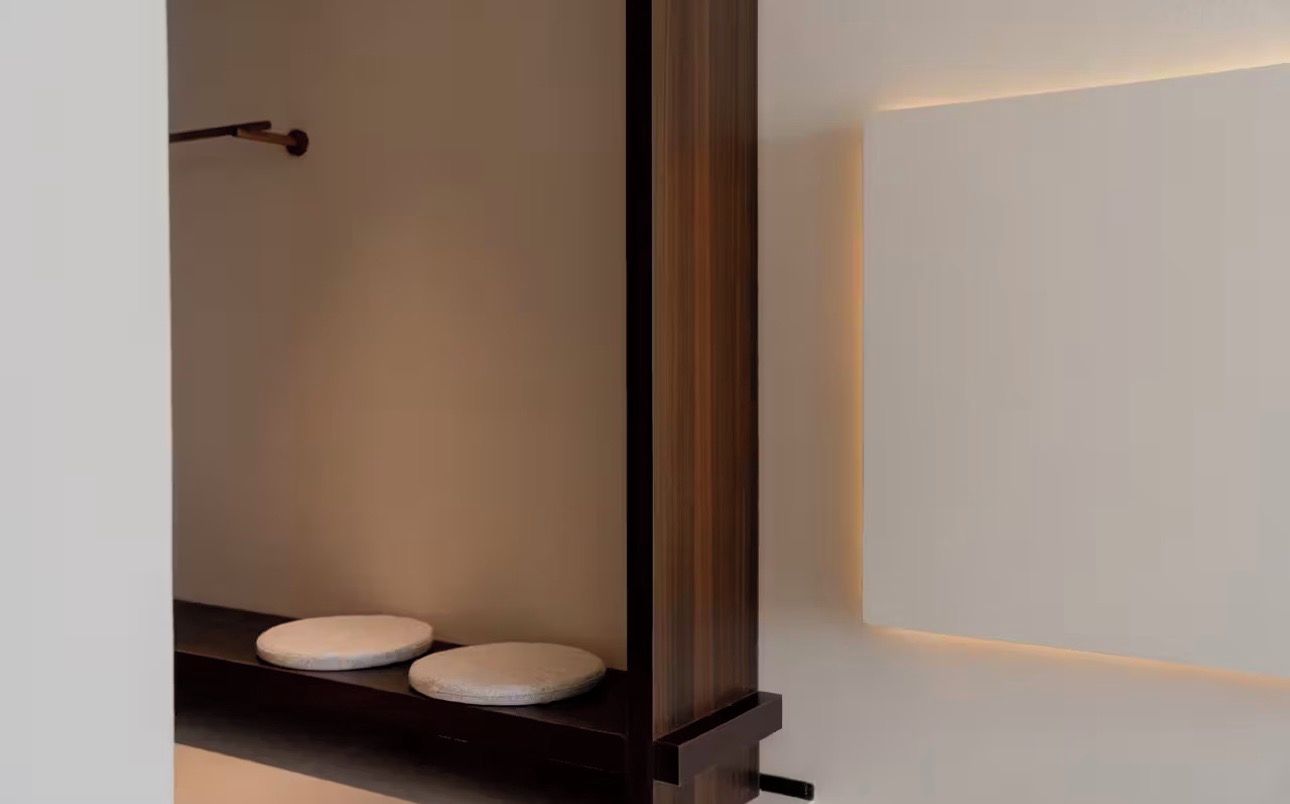 A modern bathroom with two toilets, a wooden partition, and a wall-mounted light fixture.