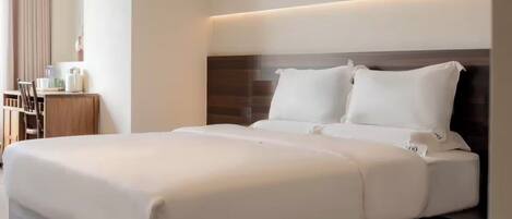A neatly made bed with a headboard, a bedside table with a lamp, and a window with curtains.
