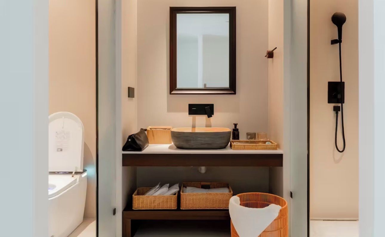 A compact bathroom with a toilet, a sink with a vessel basin, a mirror, and a shower.