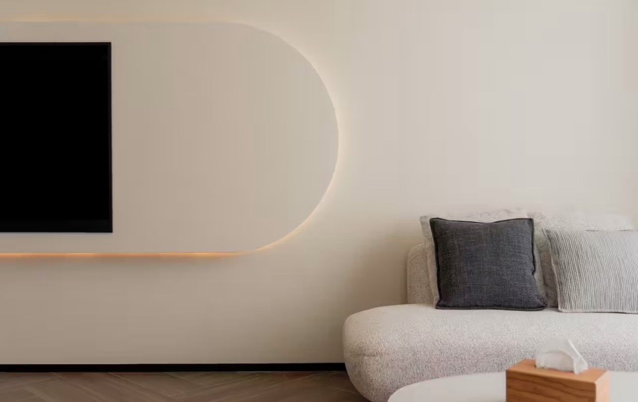 Una sala de estar moderna con un sofá, un televisor montado en la pared y una mesita de madera.