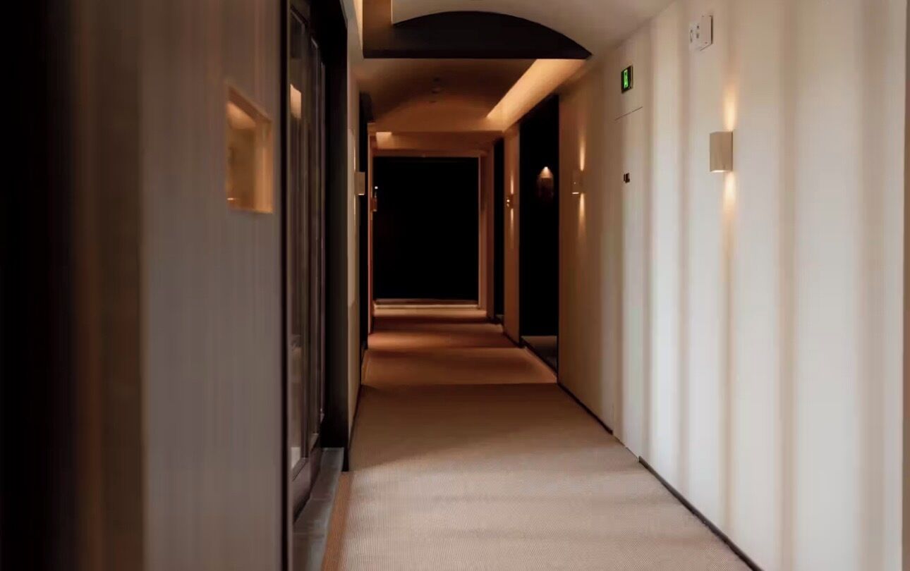 Een hotelgang met vloerbedekking, wandlampen en een nooduitgangbord.