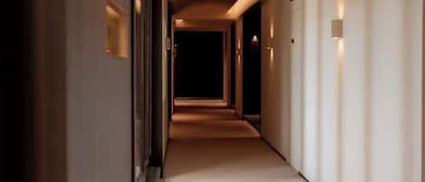 A hotel corridor with a carpeted floor, walls with light fixtures, and an emergency exit sign.