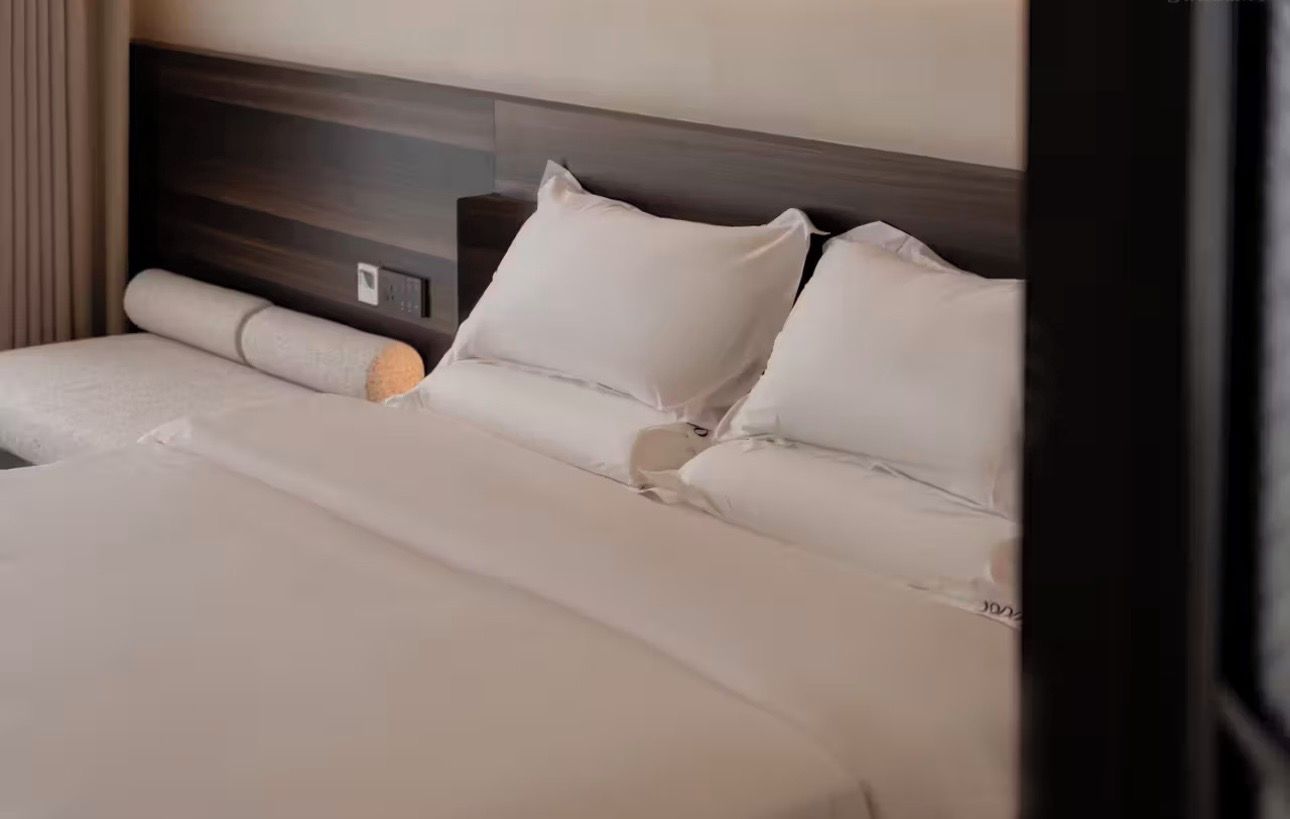 Een hotelkamer met een groot bed, een houten hoofdeinde en een nachtkastje met een lamp.