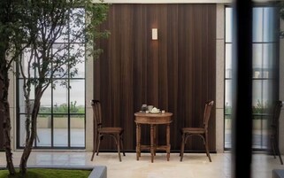 A modern interior with a dark wooden partition, a round wooden table with chairs, and a view through a glass door.