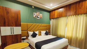 A hotel room with a bed, a wooden wardrobe, a small table, and a curtain.