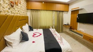 A hotel room with a bed, a television, a wooden headboard, a wall-mounted TV, and a curtain.