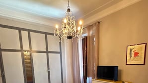 Ein Schlafzimmer mit einem großen Bett, einem Fernseher auf einem Schreibtisch, einer Kristallleuchtre und einem Schiebetürenschrank.