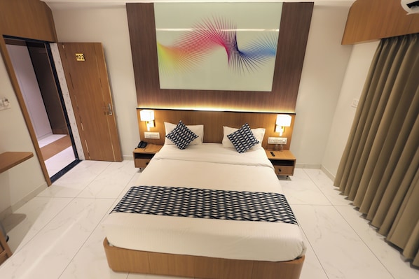Une chambre d’hôtel avec un grand lit, deux tables de chevet, un téléviseur fixé au mur et une porte portant un numéro.