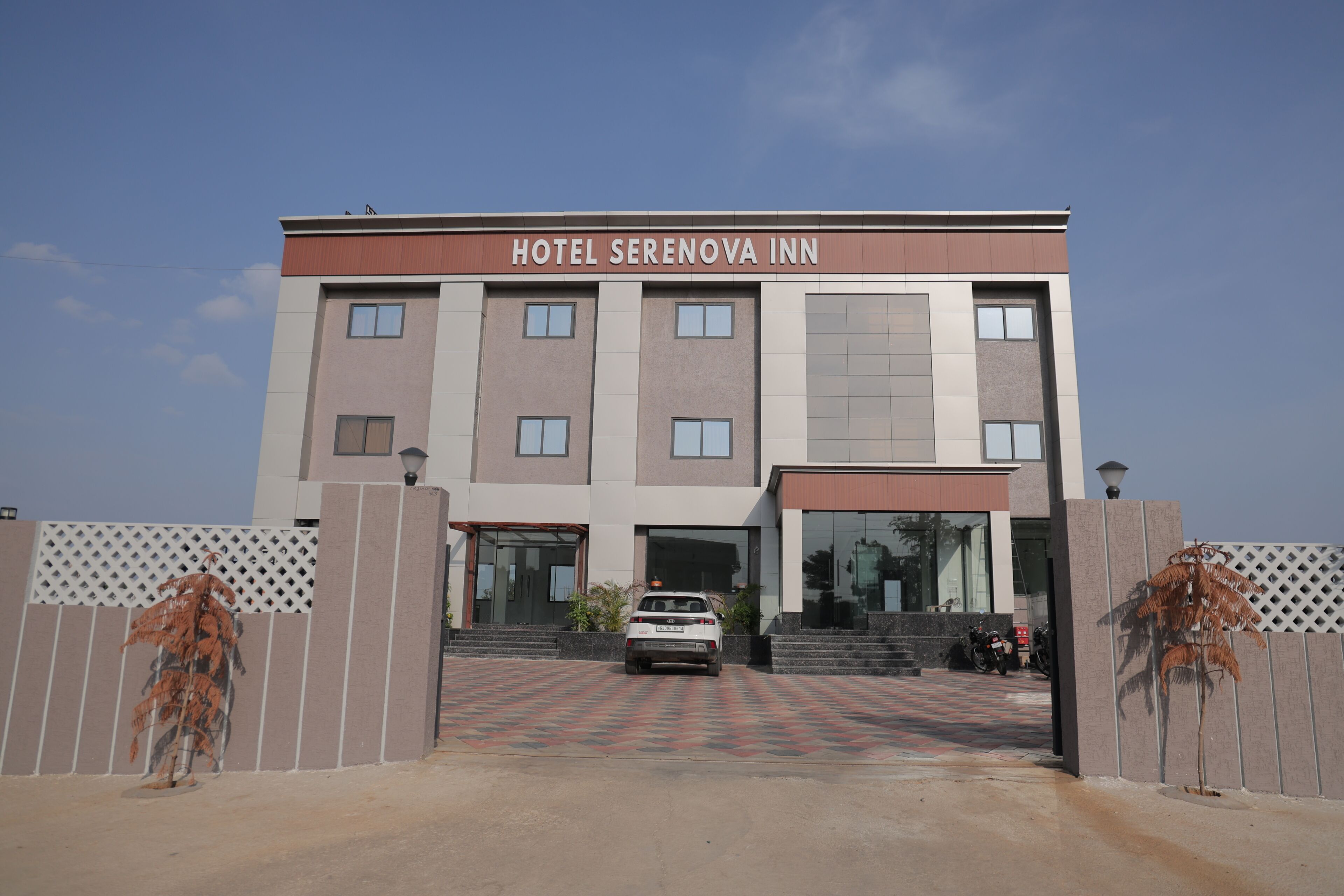A hotel named SERENOVA INN with a modern facade, a car parked in front, and a paved entrance area.