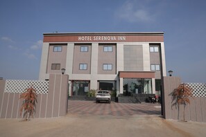 A hotel named SERENOVA INN with a modern facade, a car parked in front, and a paved entrance area.