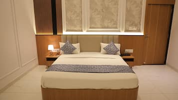 A bedroom with a large bed, two bedside tables, a nightstand, a lamp, and a window with a view.