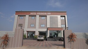 Un hotel llamado 'Hotel Serenova Inn' con una fachada moderna, un coche estacionado frente al establecimiento y un cielo despejado.