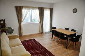 A living room with a sofa, a dining table with chairs, a rug, and a window with curtains.