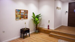 A hallway with a bulletin board, a potted plant, a fire extinguisher, and a wooden floor.