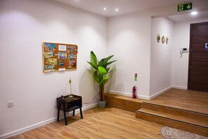 A hallway with a bulletin board, a potted plant, a fire extinguisher, and a wooden floor.