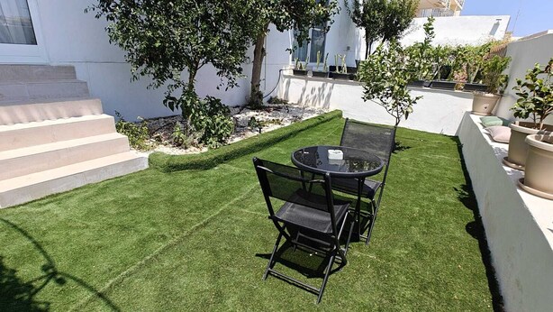 A patio with a table and chairs, surrounded by a well-manicured lawn and potted plants.
