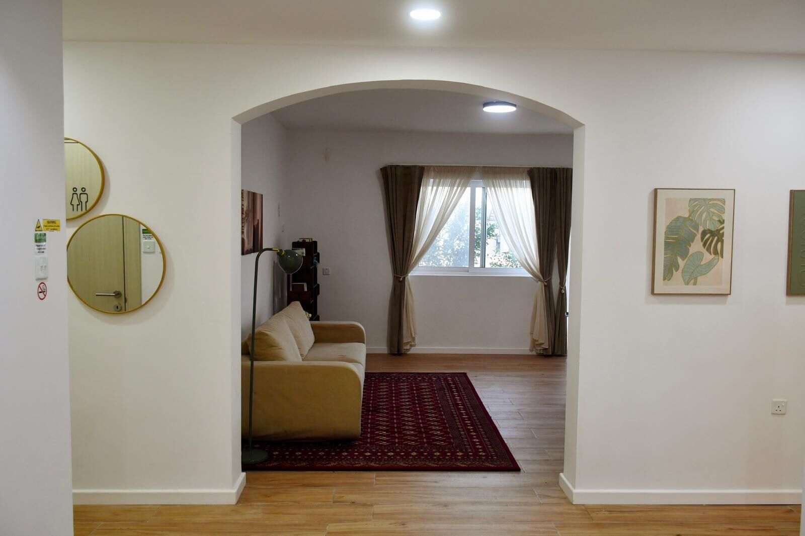 Una sala de estar con un sofá, un tapete rojo, una ventana con cortinas y espejos en la pared.