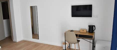 A room with a wooden desk, a chair, a flat-screen TV mounted on the wall, a small white appliance, and a mirror.