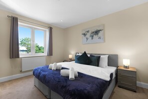 A bedroom with a large bed, two bedside tables, a world map artwork, and a window with curtains. - Heathrow Living Apartments by 360 Stays - Apt 08 (Stanwell)