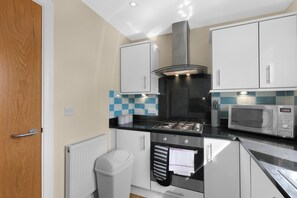 A compact kitchen with a gas stove, a microwave, and white cabinets. - Heathrow Living Apartments by 360 Stays - Apt 08 (Stanwell)