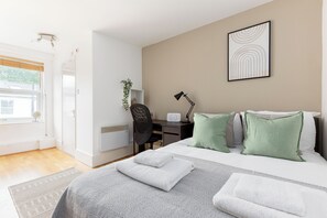 A modern bedroom with a bed, desk, chair, and a view of the outdoors. - Cosy studio Apartment near Hyde Park (London)