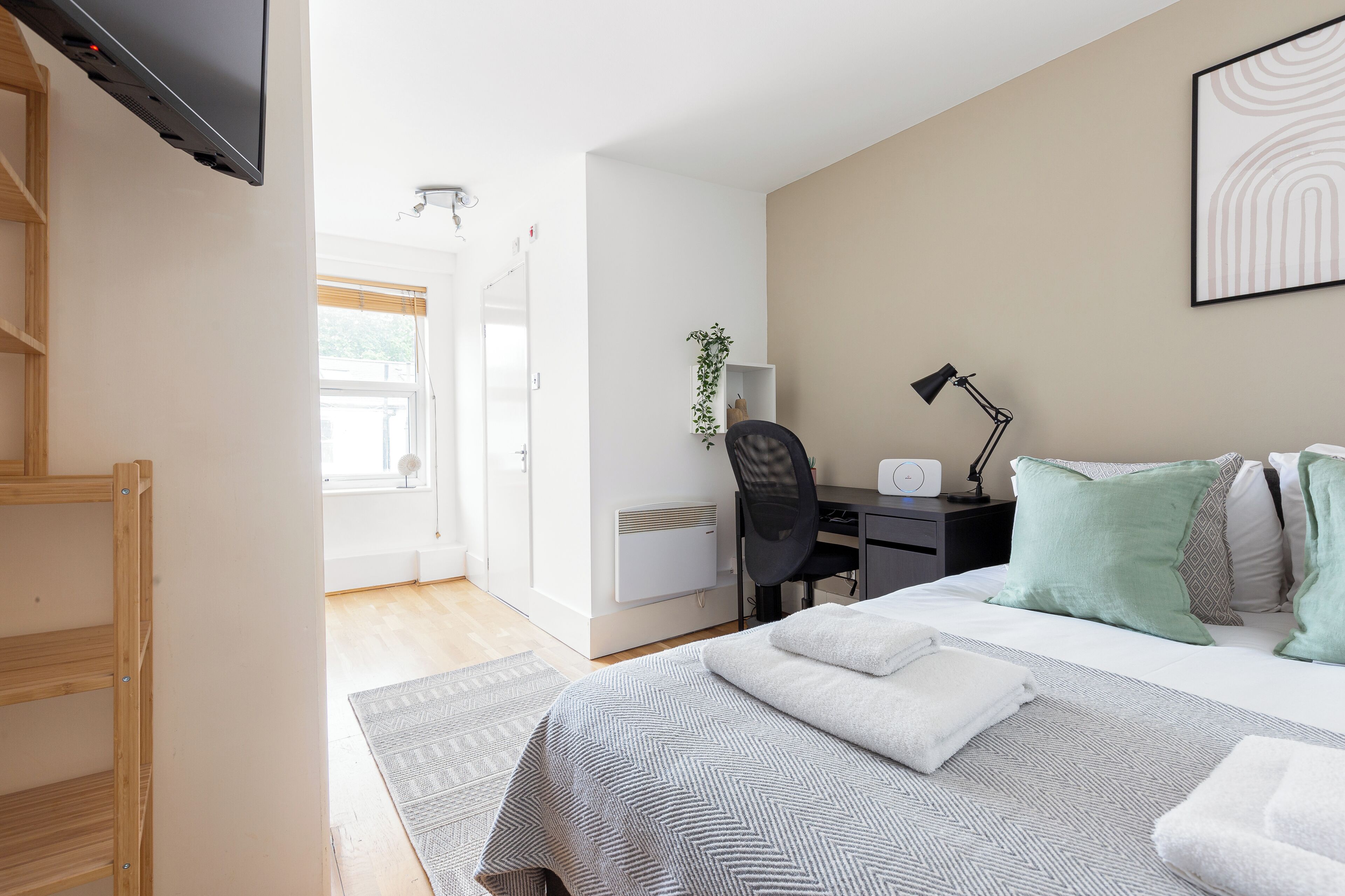 A modern hotel room with a bed, desk, chair, and a television.