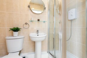 A bathroom with a toilet, sink, shower, and a mirror. - Cosy studio Apartment near Hyde Park (London)