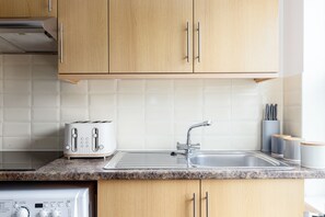 A kitchen with wooden cabinets, a stainless steel sink, a toaster, and a dishwasher. - Cosy studio Apartment near Hyde Park (London)