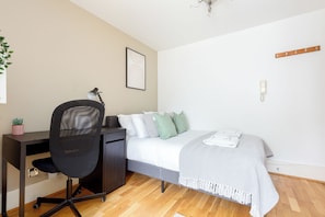 Ein Schlafzimmer mit Bett, Schreibtisch, Stuhl und einem kleinen Topfpflanzen.