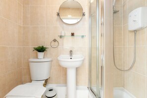 Ein Badezimmer mit Toilette, Waschbecken, Spiegel, Dusche und einer Glasablage mit Toilettenartikeln.