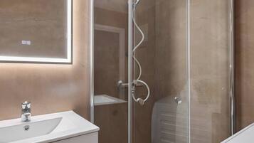 A modern bathroom with a glass shower enclosure, a white sink, and a mirror.