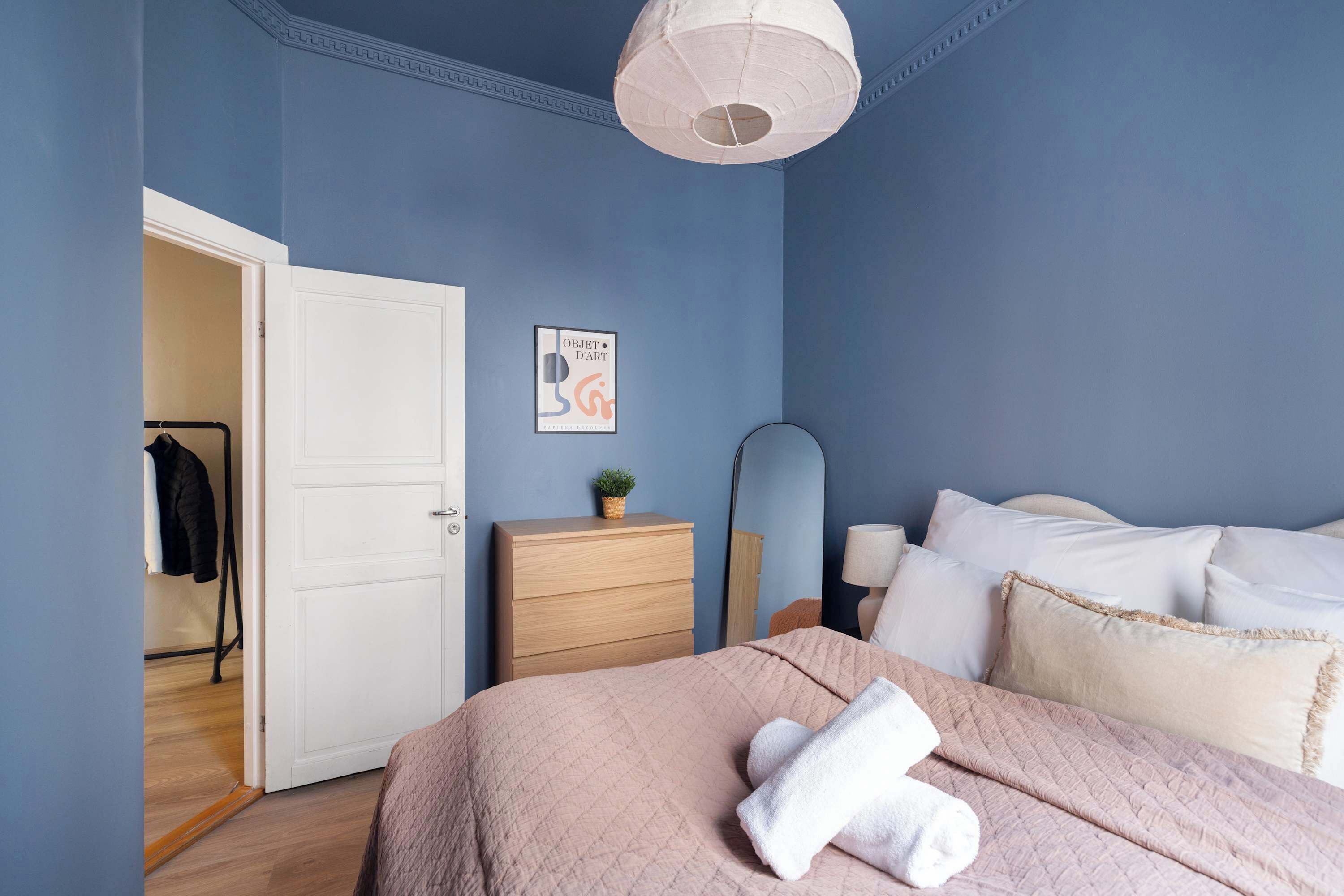 A bedroom with a bed, a dresser, a mirror, and a door leading to another room.