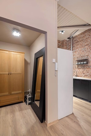 Une pièce avec une armoire en bois, un miroir, un coin cuisine avec un mur en briques et une porte blanche.