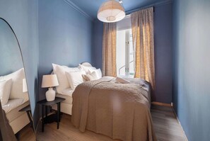 Une chambre à coucher avec un lit, une chaise, une table de chevet et une fenêtre avec des rideaux.