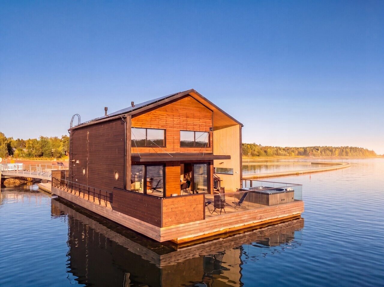 A modern houseboat with a deck, large windows, and a hot tub.