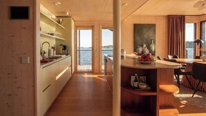 A modern kitchen with a view of the water, wooden flooring, and a dining area with a table and chairs. - Stay North - Loviisa Floating House (Loviisa)