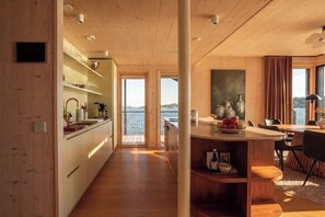 A modern kitchen with a view of the water, wooden flooring, and a dining area with a table and chairs. - Stay North - Loviisa Floating House (Loviisa)