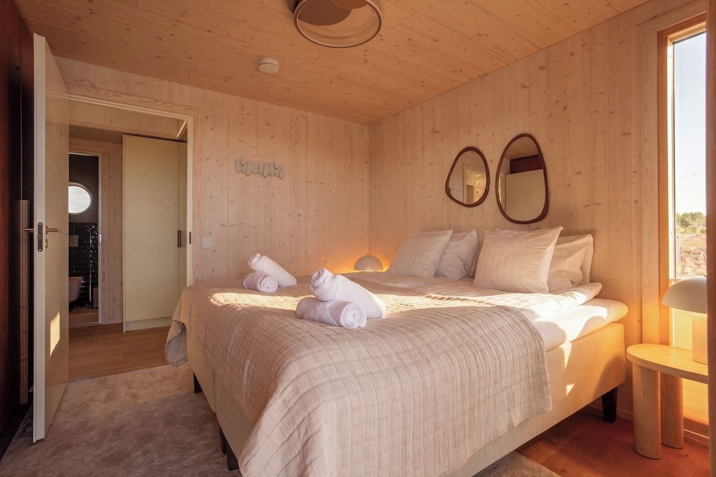 A wooden-paneled bedroom with a bed, two wall mirrors, and a bedside table.