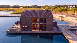 A modern houseboat with a hot tub, outdoor seating, and a view of a lake and forest. - Stay North - Loviisa Floating House (Loviisa)