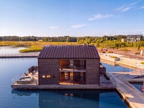A modern houseboat with a hot tub, outdoor seating, and a view of a lake and forest. - Stay North - Loviisa Floating House (Loviisa)