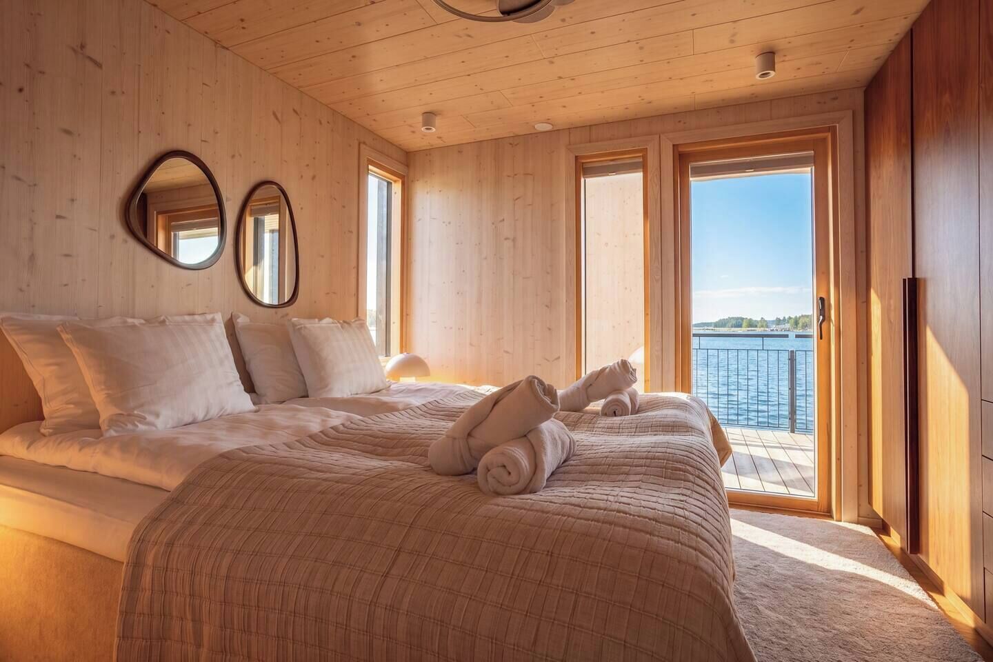 Een slaapkamer met een groot bed, twee ramen en uitzicht op het water.