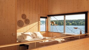 A cabin with a bed, a window, and a view of a lake. - Stay North - Loviisa Floating House (Loviisa)
